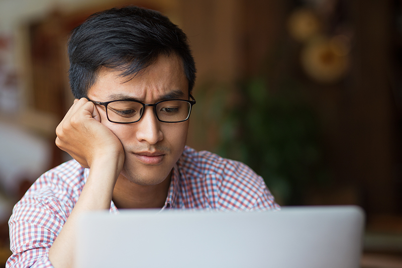 Young Asian student looking bored while taking a survey on a laptop